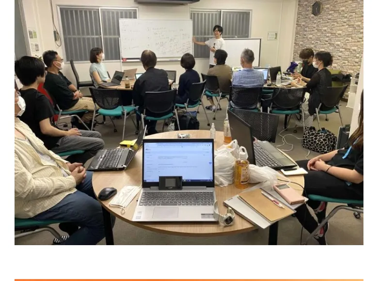 勉強会の会場で、参加者がノートパソコンを開いて講師の話を聞いている様子の写真